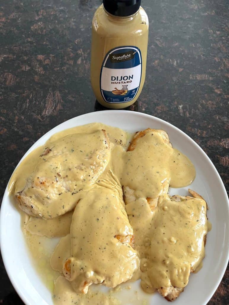 Plated Dijon Mustard Chicken topped with creamy sauce, accompanied by a bottle of Dijon mustard.