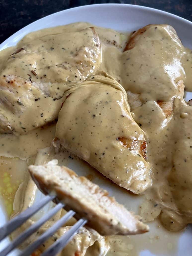 Fork showcasing a slice of perfectly cooked Dijon Mustard Chicken, highlighting the tender texture and creamy mustard sauce on a plate.