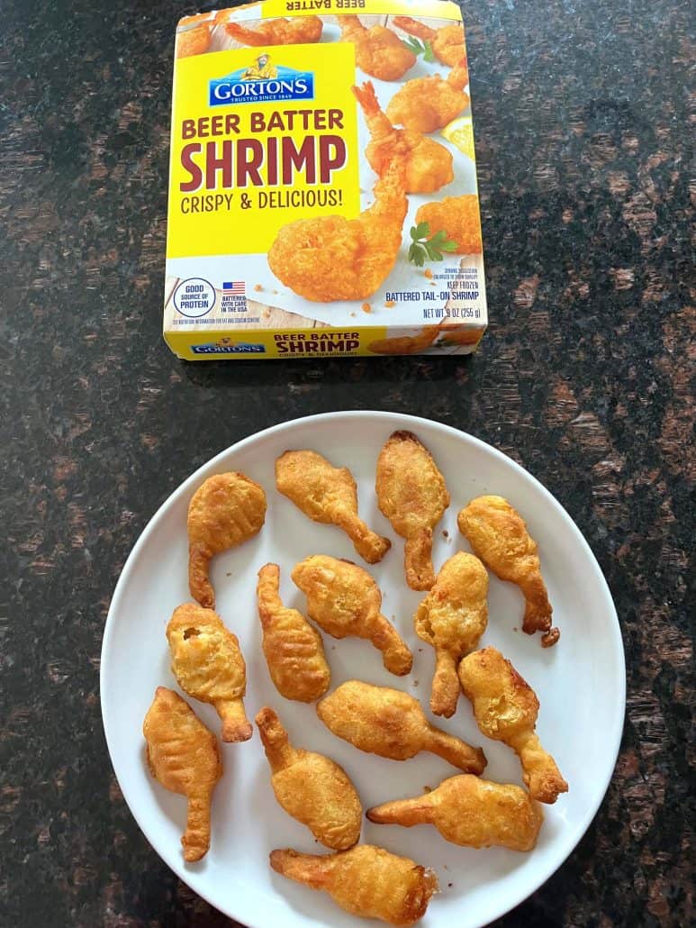 White plate filled with crispy, golden beer-battered shrimp placed below a box of Gorton's Beer Batter Shrimp, showcasing the perfectly cooked shrimp and their convenient packaging for quick and delicious meals.