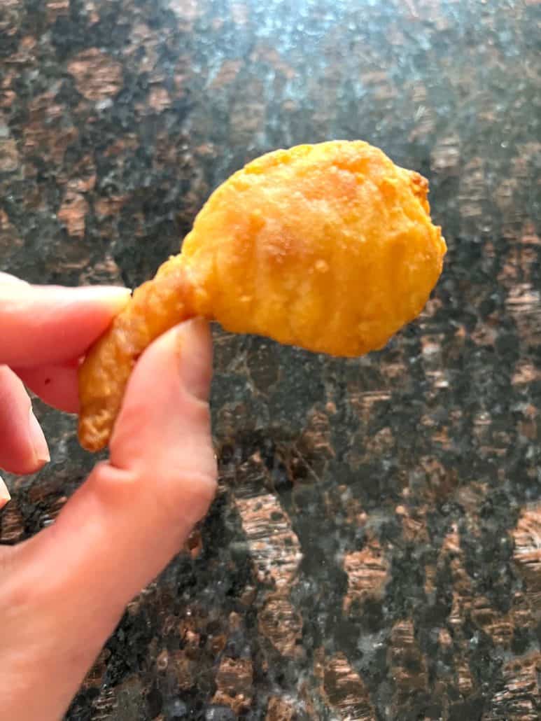 Close-up of a hand holding a single golden, crispy beer-battered shrimp, showcasing its crunchy texture and bite-sized appeal.