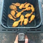 Hand holding an air fryer basket filled with golden, crispy beer-battered shrimp, showcasing their perfectly cooked texture and convenience as a quick and tasty appetizer or meal option.