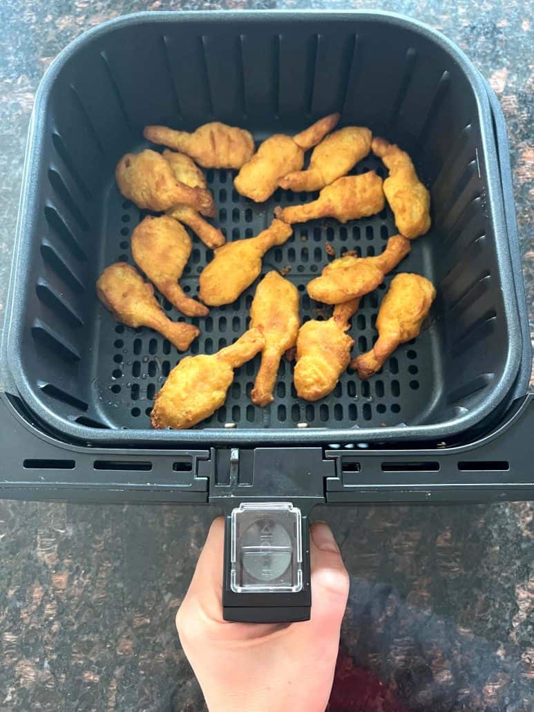 Hand holding an air fryer basket filled with golden, crispy beer-battered shrimp, showcasing their perfectly cooked texture and convenience as a quick and tasty appetizer or meal option.