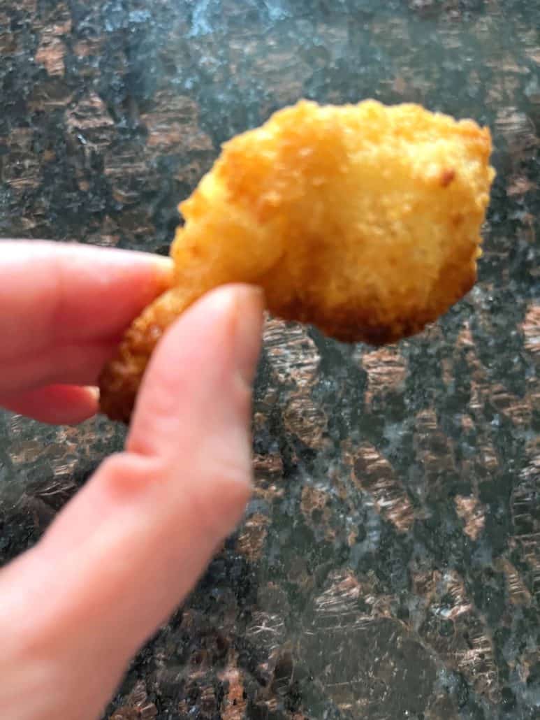 Close-up hand of Melanie Mendelson from melaniecooks.com holding a crispy, golden butterfly shrimp, showcasing its perfectly cooked texture.