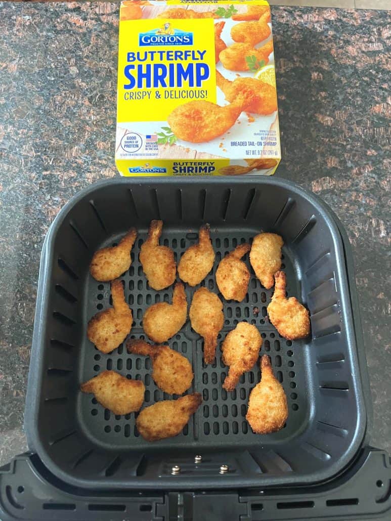 Cooked butterfly shrimp in the air fryer basket placed in front of a Gorton's Butterfly Shrimp box, showcasing the finished recipe.