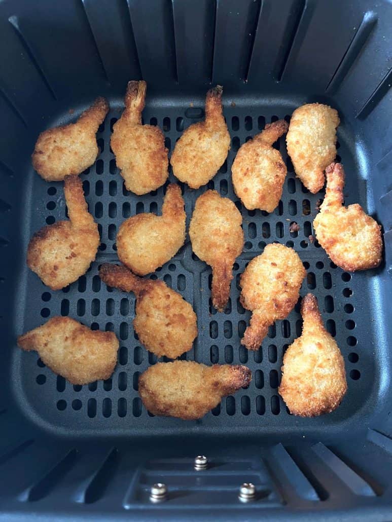 Top view of crispy golden butterfly shrimp cooked evenly in the air fryer basket.