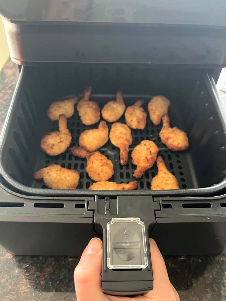 Air fryer basket with golden brown butterfly shrimp freshly cooked and ready to serve.