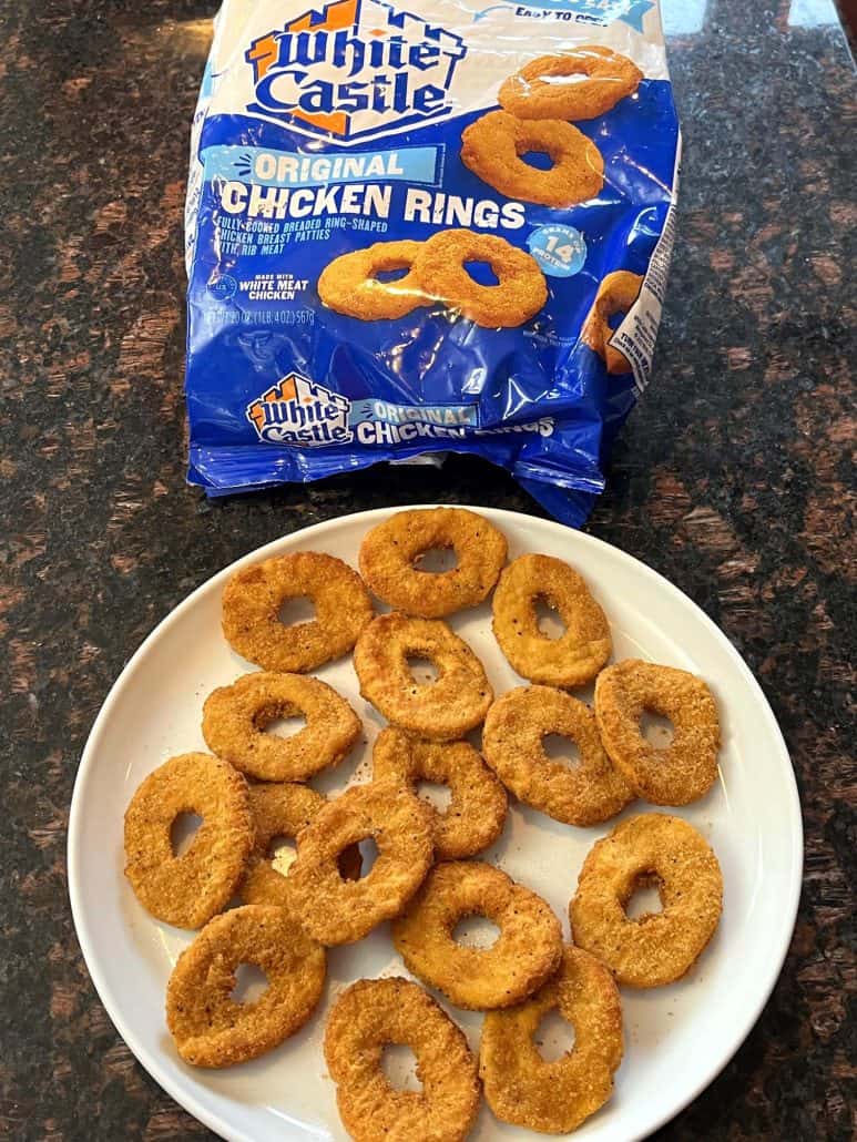 A plate full of crispy cooked, White Castle chicken rings with the package displayed in the background.