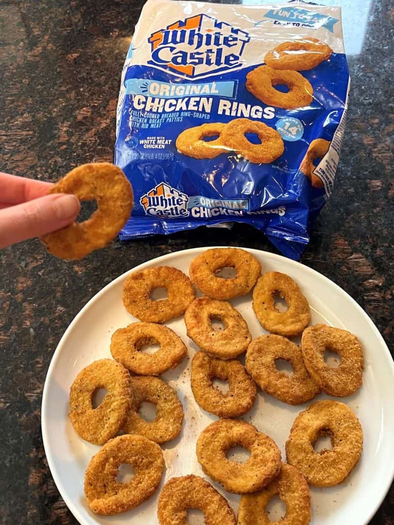 Hand of Melanie Mendelson from melaniecooks.com holding freshly cooked, crispy White Castle chicken rings, with the package displayed in the background.