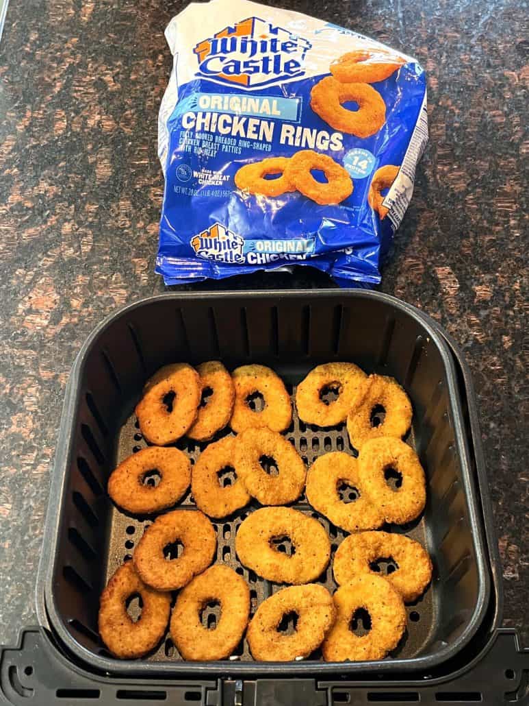 Cooked White Castle chicken rings in an air fryer basket with the package displayed in the background.