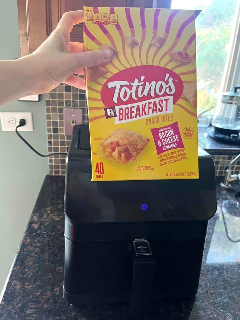 Hand of Melanie Mendelson from melaniecooks.com holding a box of Totino's Breakfast Snack Bites in front of an air fryer, ready to demonstrate how to cook them perfectly crispy in minutes.