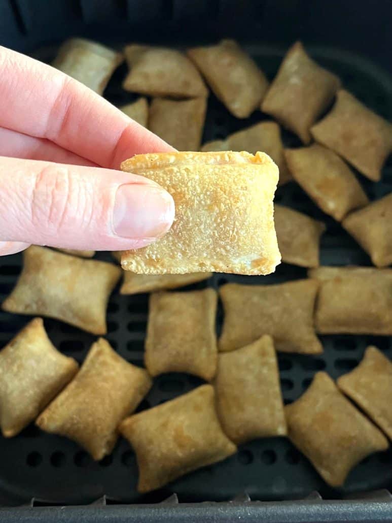 The hand of Melanie Mendelson from melaniecooks.com holding a perfectly crispy Totino's Breakfast Snack Bite with more bites visible in the air fryer basket in the background.