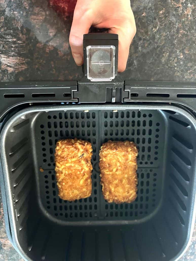 Two golden-brown Jimmy Dean stuffed hashbrowns inside an air fryer basket, freshly cooked and ready to serve.