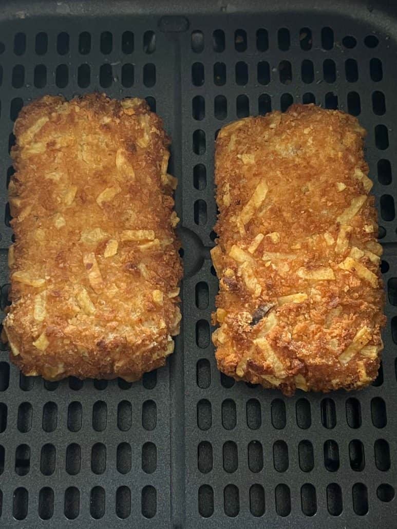 Close-up view of two golden, crispy Jimmy Dean stuffed hashbrowns sitting in an air fryer basket after cooking.