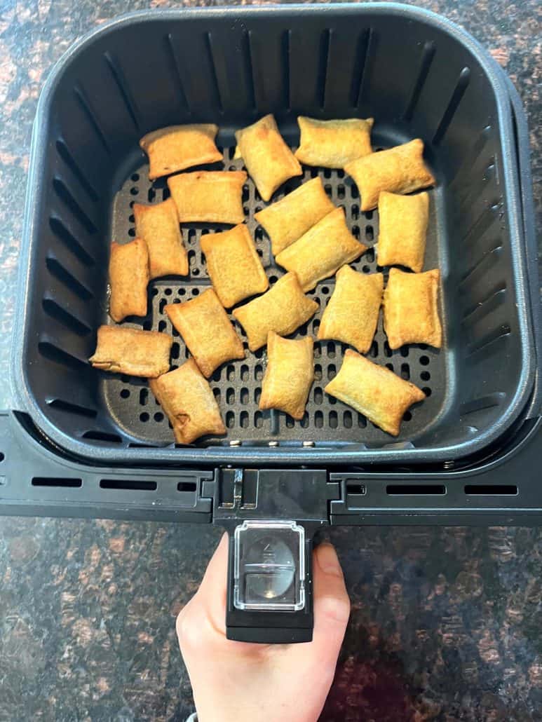 Hand of Melanie Mendelson from melaniecooks.com showing an air fryer basket filled with evenly spaced, golden-brown Air Fryer White Castle Cheeseburger Bites