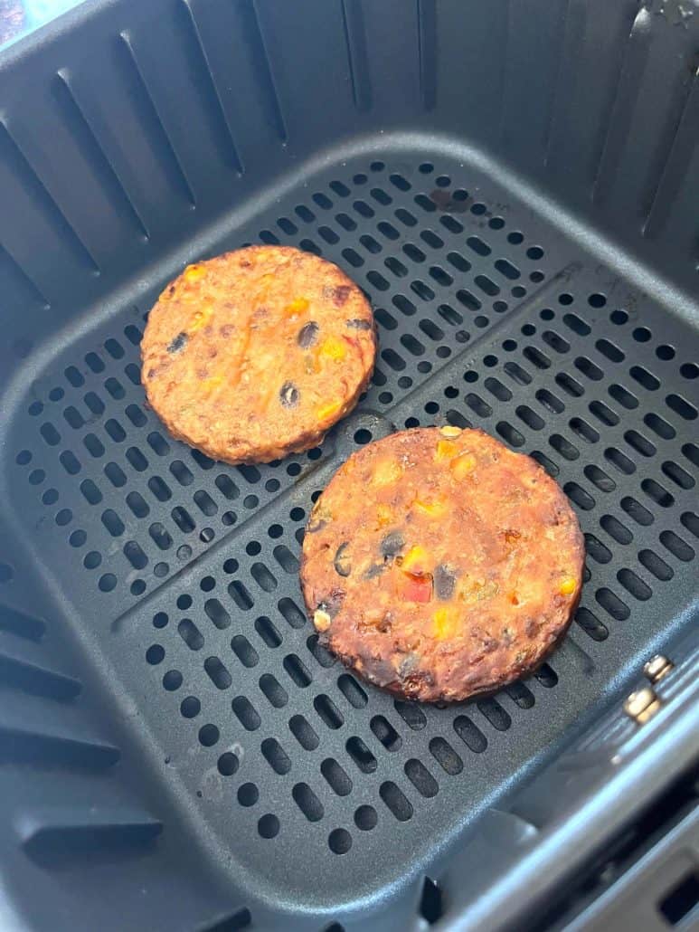Two cooked black bean burgers in an air fryer basket, showing their crispy texture after air frying from frozen.