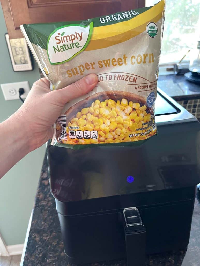Melanie Mendelson from melaniecooks.com holding a bag of frozen super sweet corn over an air fryer, ready to cook.