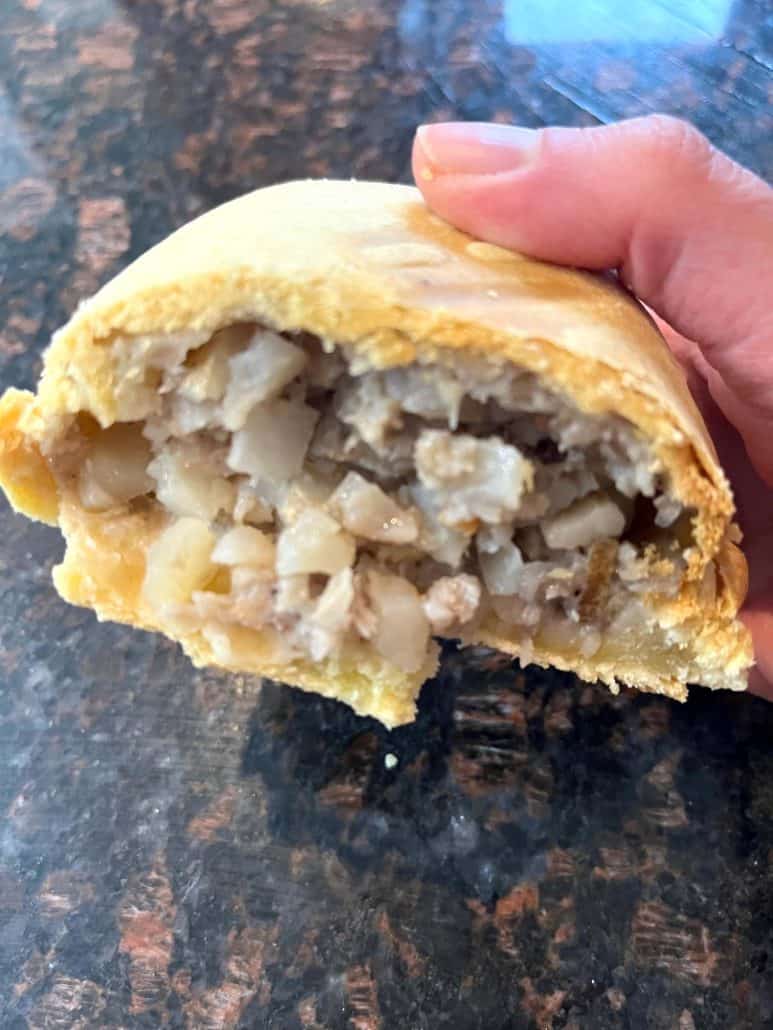 Melanie Mendelson from melaniecooks.com holding a freshly air-fried pasty cut in half, showcasing its flaky crust.