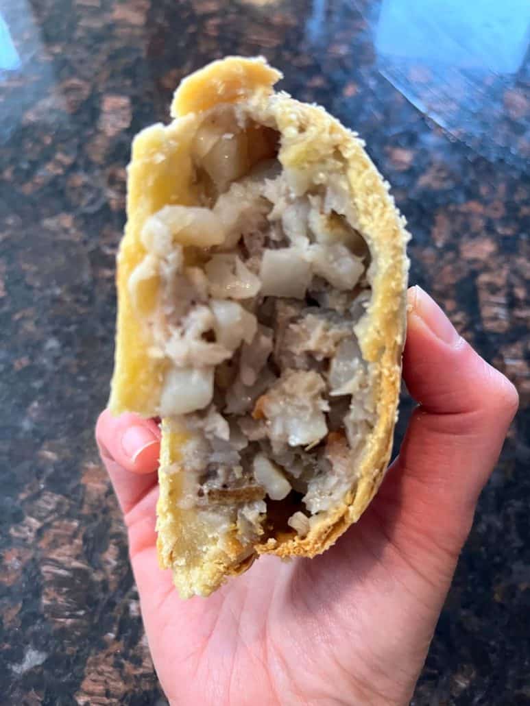 Melanie Mendelson from melaniecooks.com holding a half freshly air-fried pasty, revealing its warm, savory filling of potatoes and meat inside a crispy, golden crust.