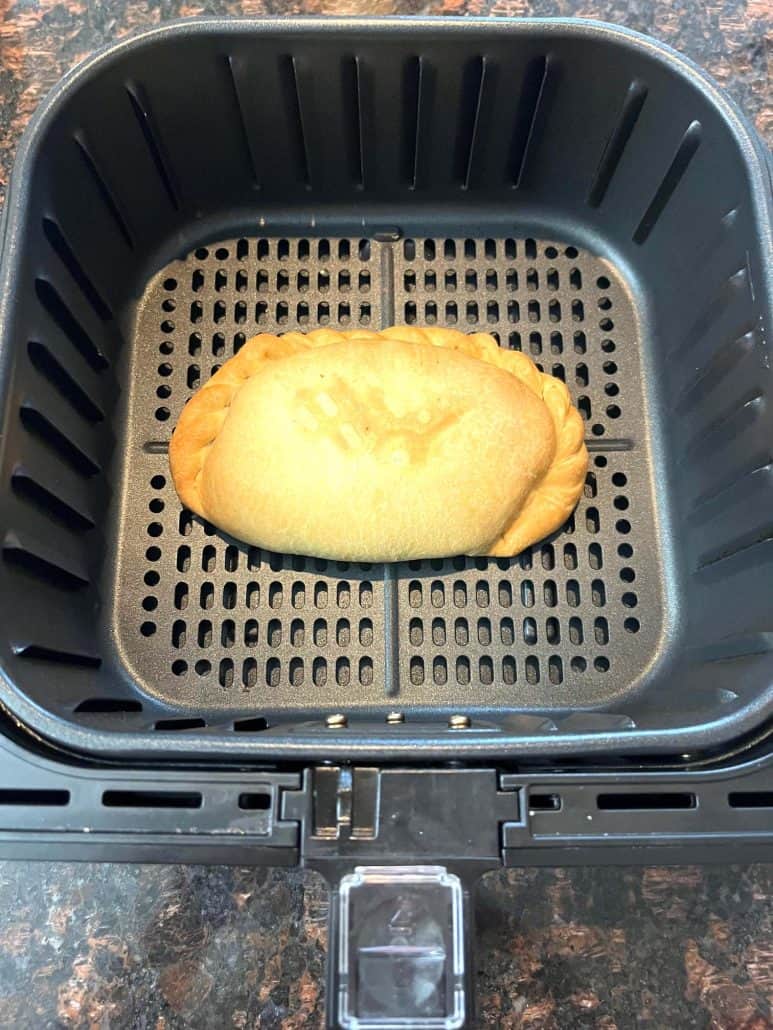 A crispy, golden-brown pasty sitting in an air fryer basket after cooking.