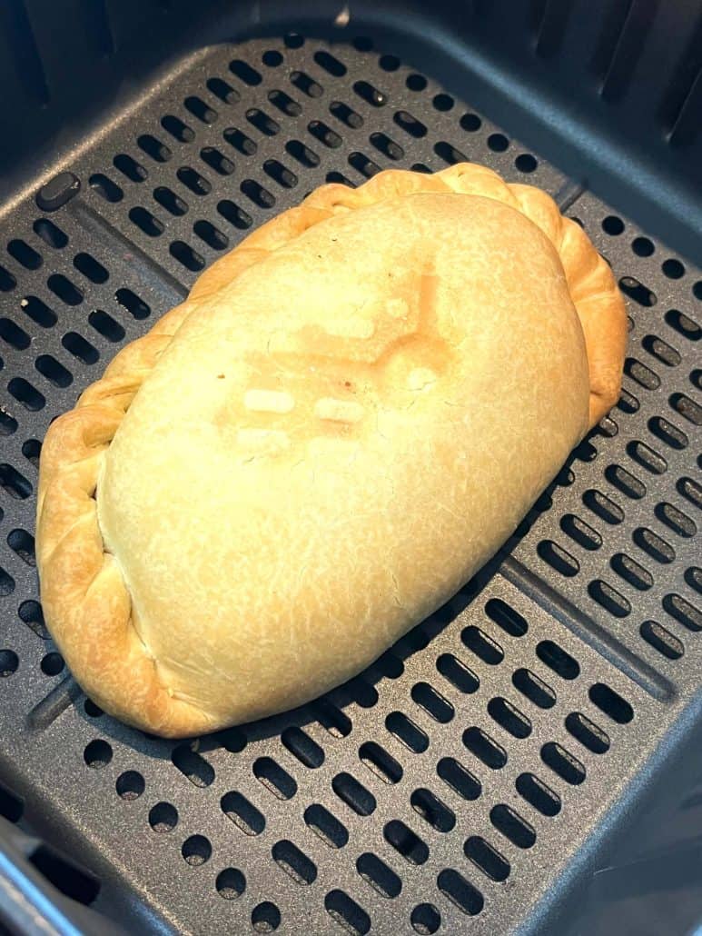 A close-up of a golden-brown pasty in an air fryer basket, showing its crispy and flaky texture.