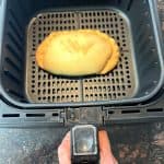 Air fryer basket with a golden-brown frozen pasty cooking inside, showing how easy it is to make a crispy and flaky pasty using an air fryer.