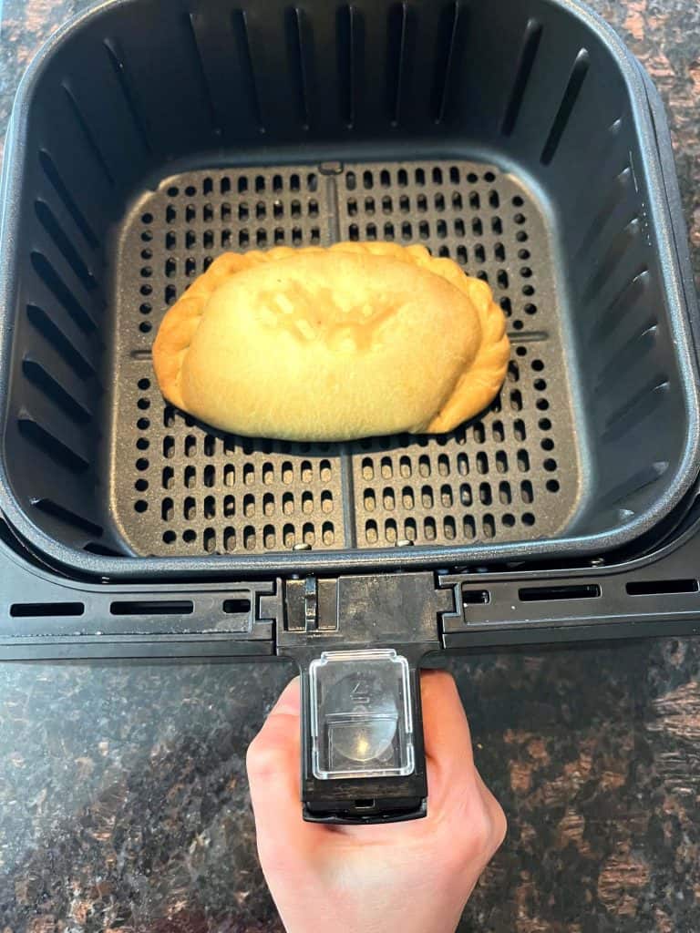 Air fryer basket with a golden-brown frozen pasty cooking inside, showing how easy it is to make a crispy and flaky pasty using an air fryer.