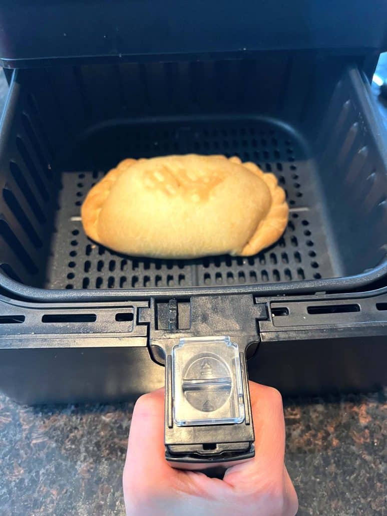 A golden-brown pasty inside an air fryer basket, freshly cooked and ready to be served.