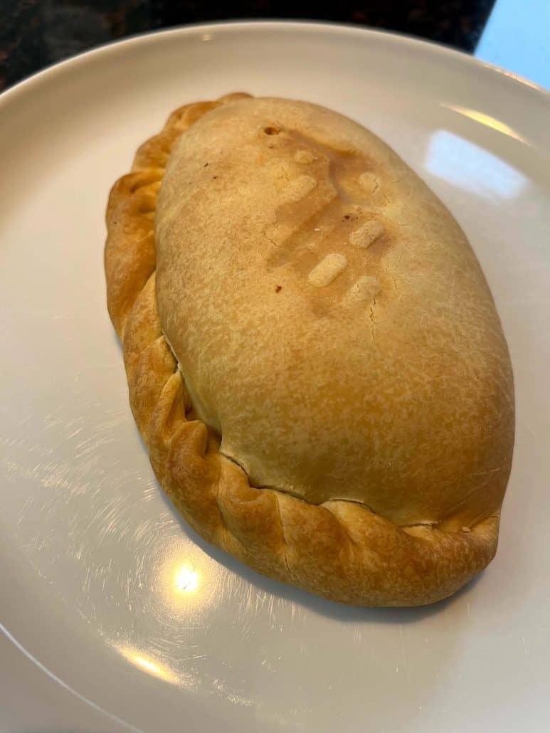 Ready to eat crispy, golden-brown pasty on a white plate.