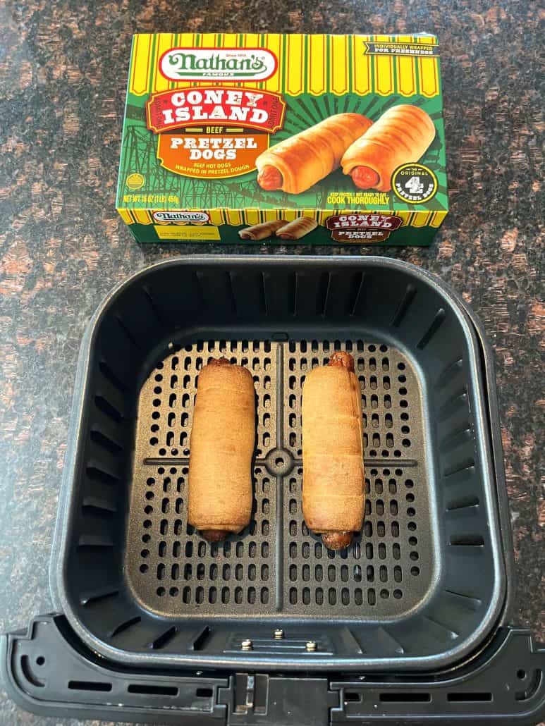 Air fryer basket with two cooked pretzel dogs, with a box of Nathan’s Coney Island frozen pretzel dogs in the background.