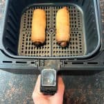 Air fryer basket with two golden-brown pretzel dogs, freshly cooked and ready to be served.