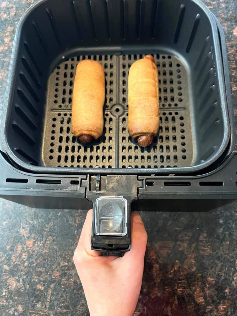 Air fryer basket with two golden-brown pretzel dogs, freshly cooked and ready to be served.