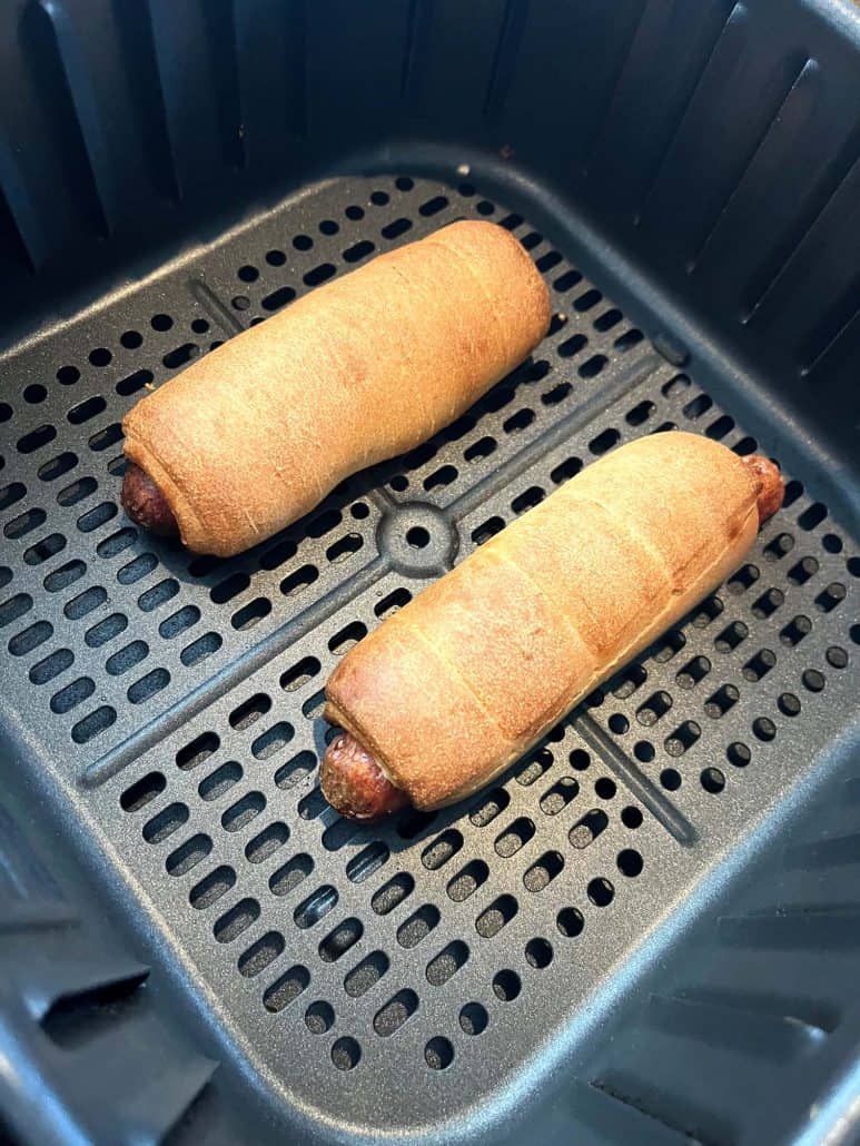 Close-up of two golden-brown pretzel dogs in an air fryer basket, freshly cooked and ready to eat.