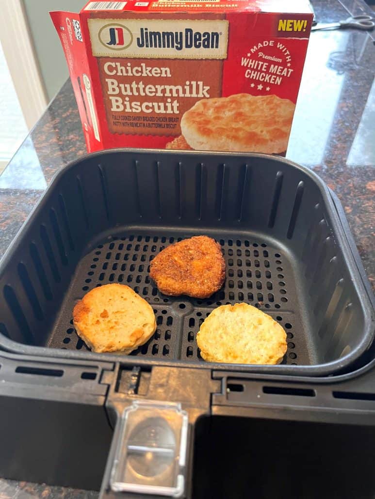 Air fryer basket with Jimmy Dean Chicken Buttermilk Biscuit sandwich, with the product box in the background.