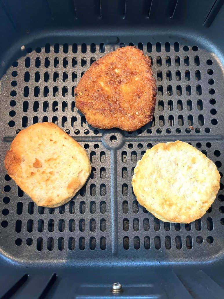 Close-up of an air fryer basket with three Jimmy Dean Chicken Buttermilk Biscuit sandwich components cooking until golden and crispy.