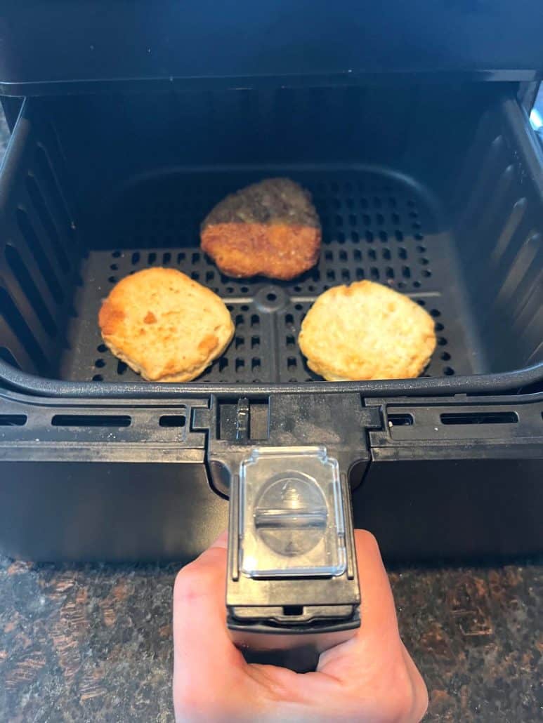 Air fryer basket with three Jimmy Dean Chicken Buttermilk Biscuit sandwich patties cooking to crispy perfection.