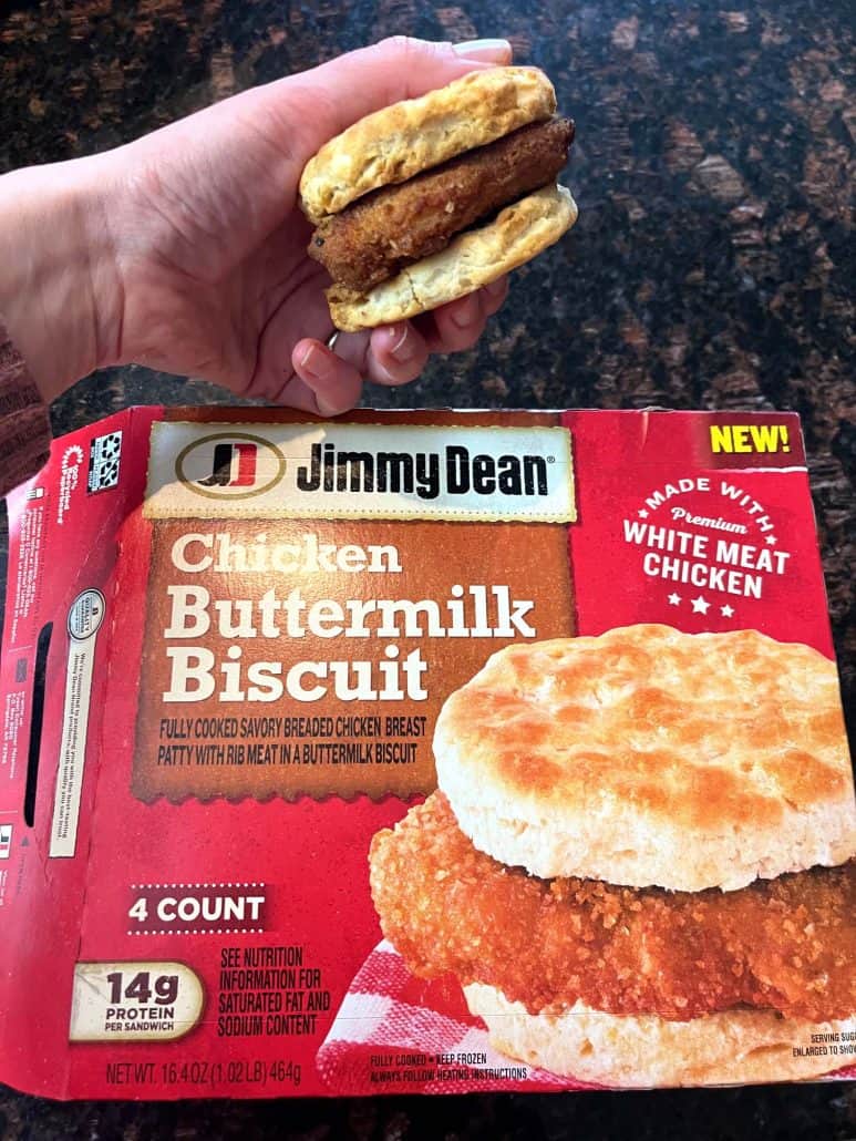 Melanie Mendelson from melaniecooks.com holding a perfectly cooked, Jimmy Dean Chicken Buttermilk Biscuit Sandwich over the product box.