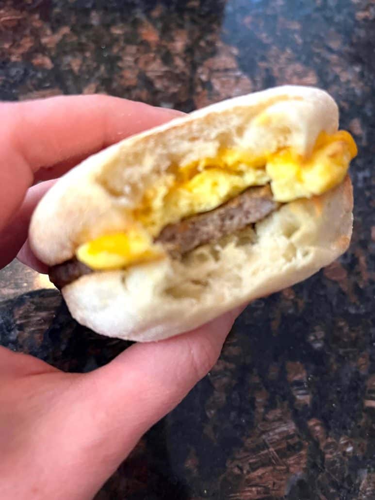 Close-up of a bitten Jimmy Dean English Muffin Sandwich, showing the fluffy egg, melted cheese, and sausage inside the perfectly toasted muffin.