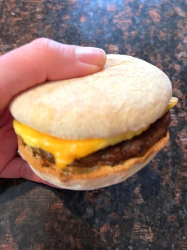 Hand of Melanie Mendelson from melaniecooks.com, holding a freshly cooked Jimmy Dean English muffin sandwich with sausage, egg, and melted cheese, made crispy in the air fryer.