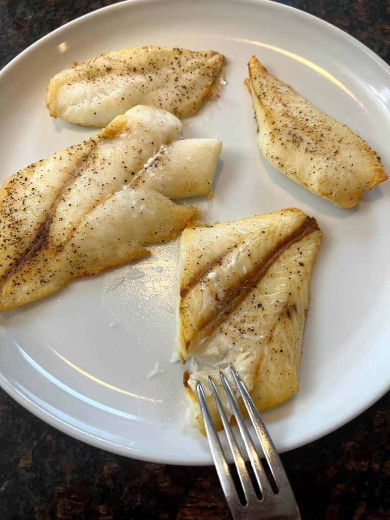 Flaky air-fried orange roughy fillet on a plate, with a fork gently pulling it apart to reveal its tender texture.