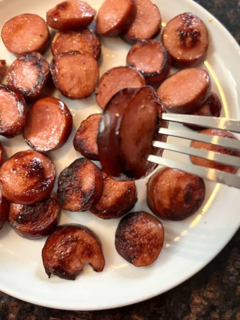 A fork holding a crispy, golden-brown air-fried ring bologna slice over a plate.