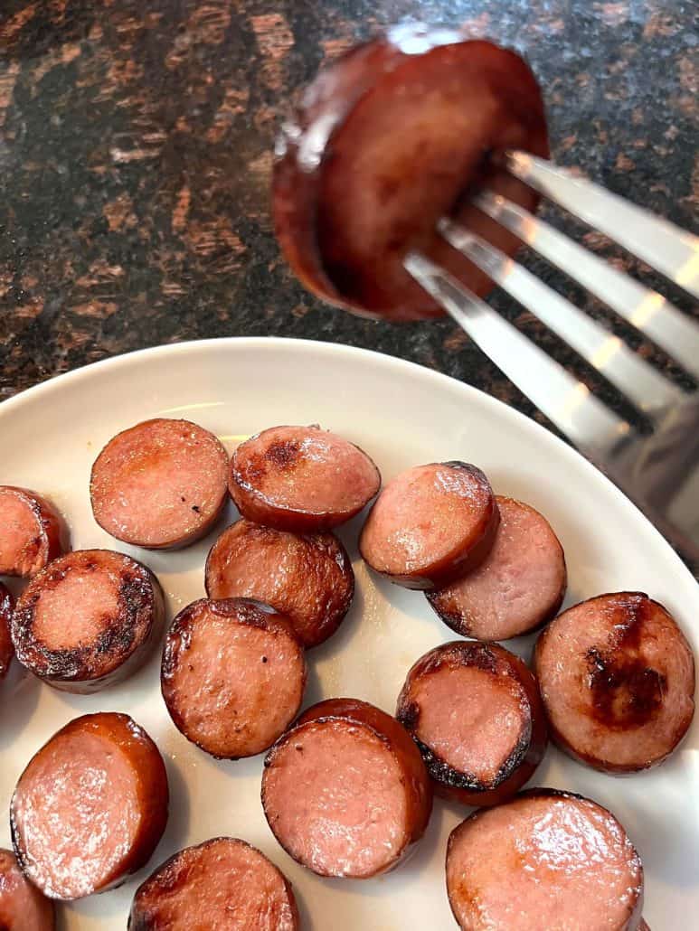 A fork lifting a crispy, air-fried ring bologna slice above a plate filled with golden-brown pieces.