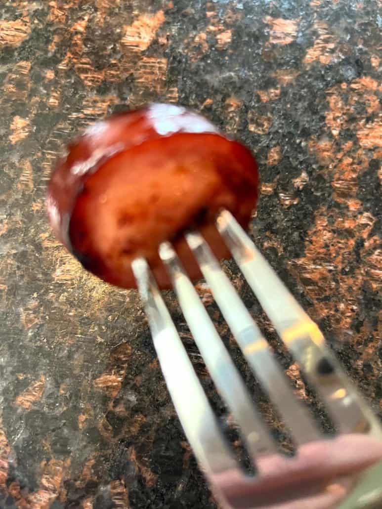 A close-up of a crispy, air-fried ring bologna slice on a fork, showcasing its golden-brown, perfectly cooked texture.