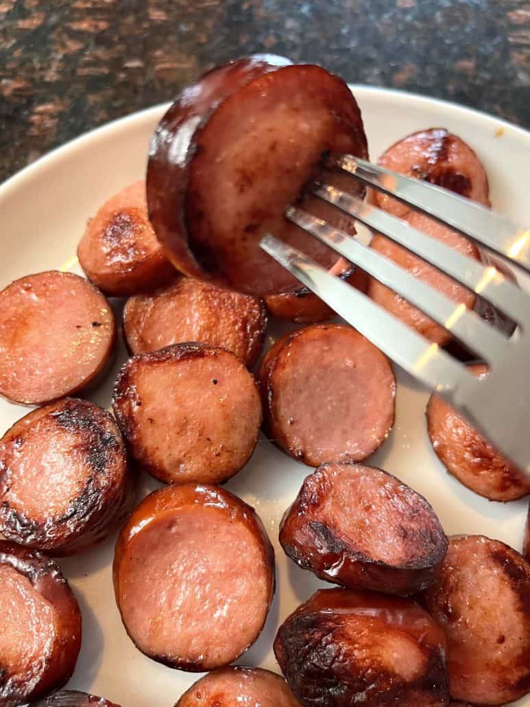 A fork holding a crispy, golden-brown air-fried ring bologna slice above a plate full of deliciously cooked pieces.