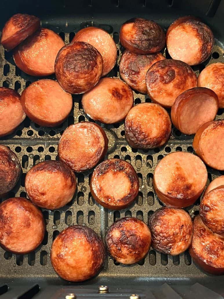 Close-up of crispy, golden-brown ring bologna slices in an air fryer basket.