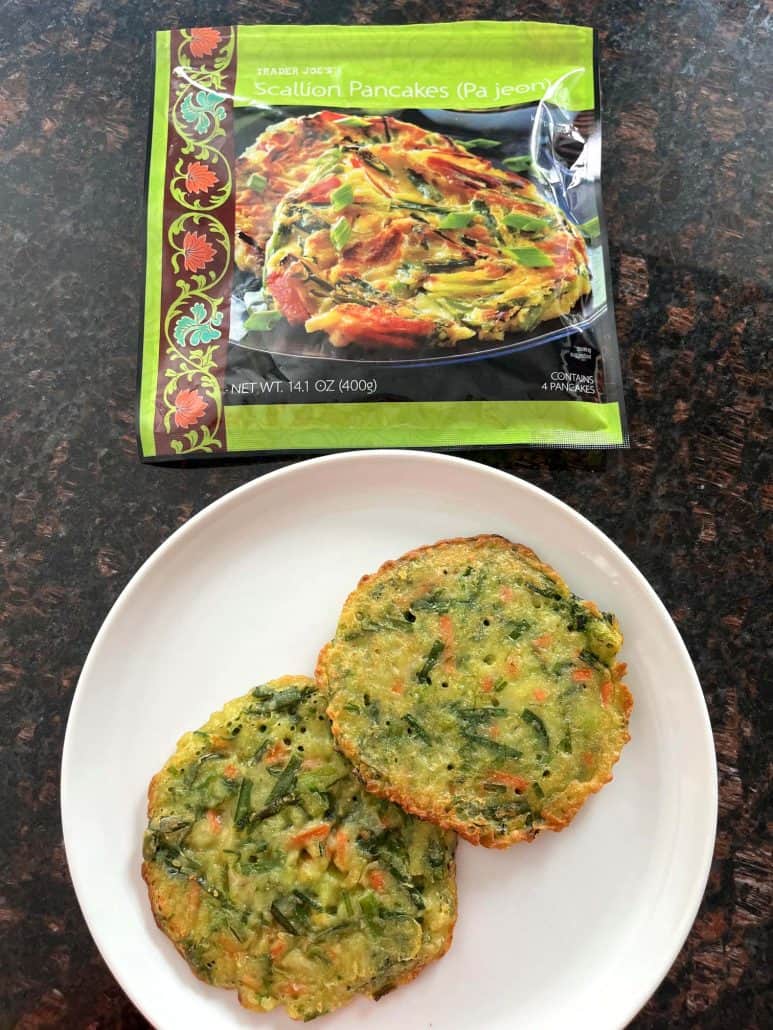 Two cooked Trader Joe’s scallion pancakes served on a white plate with the empty package shown in the background, ready to enjoy after air frying.