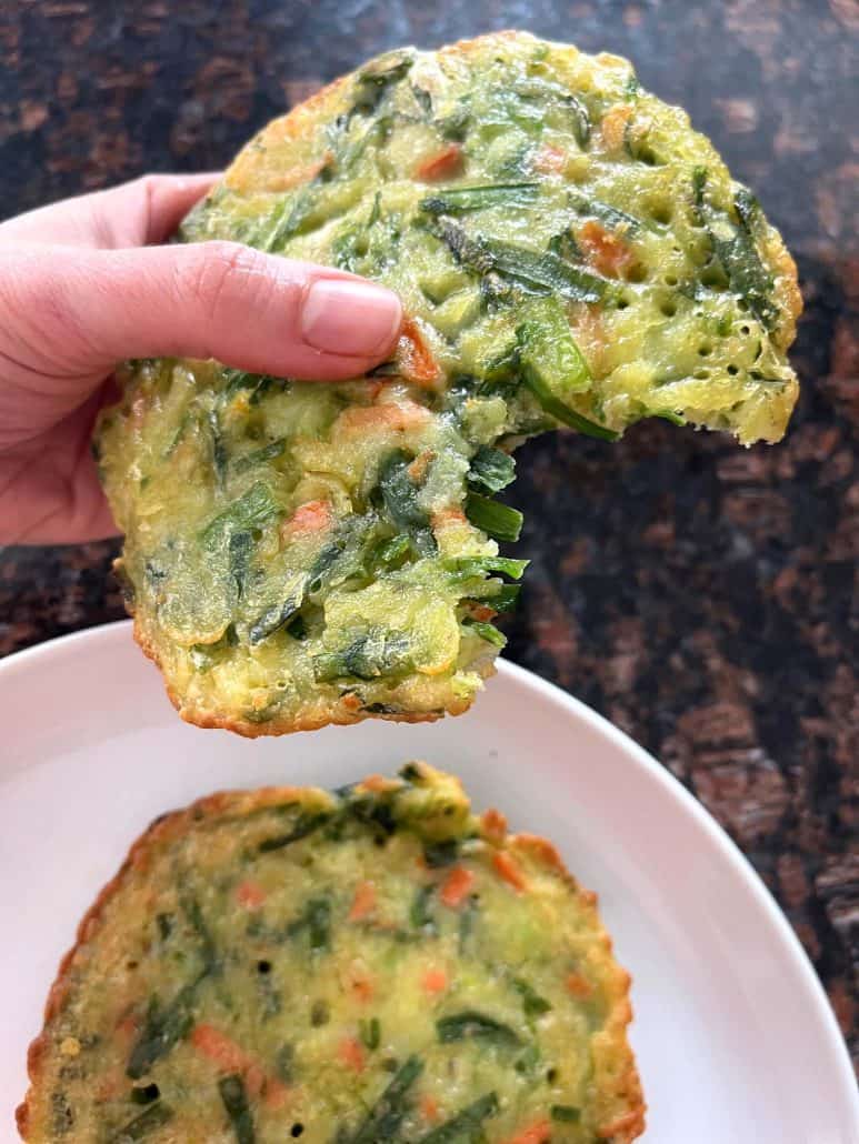 Melanie Mendelson from melaniecooks.com holding a Trader Joe’s scallion pancake with a bite taken out, showing the soft and savory inside.