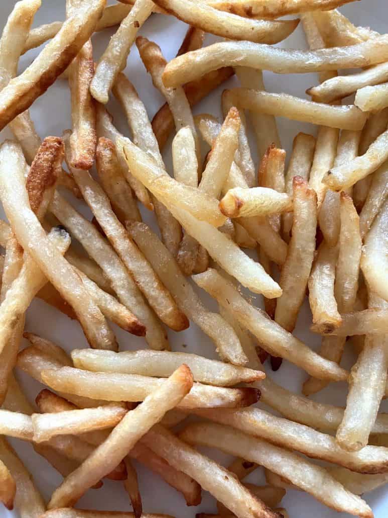 Close-up of golden and crispy McCain Beer Battered Fries on a white plate, highlighting their texture.