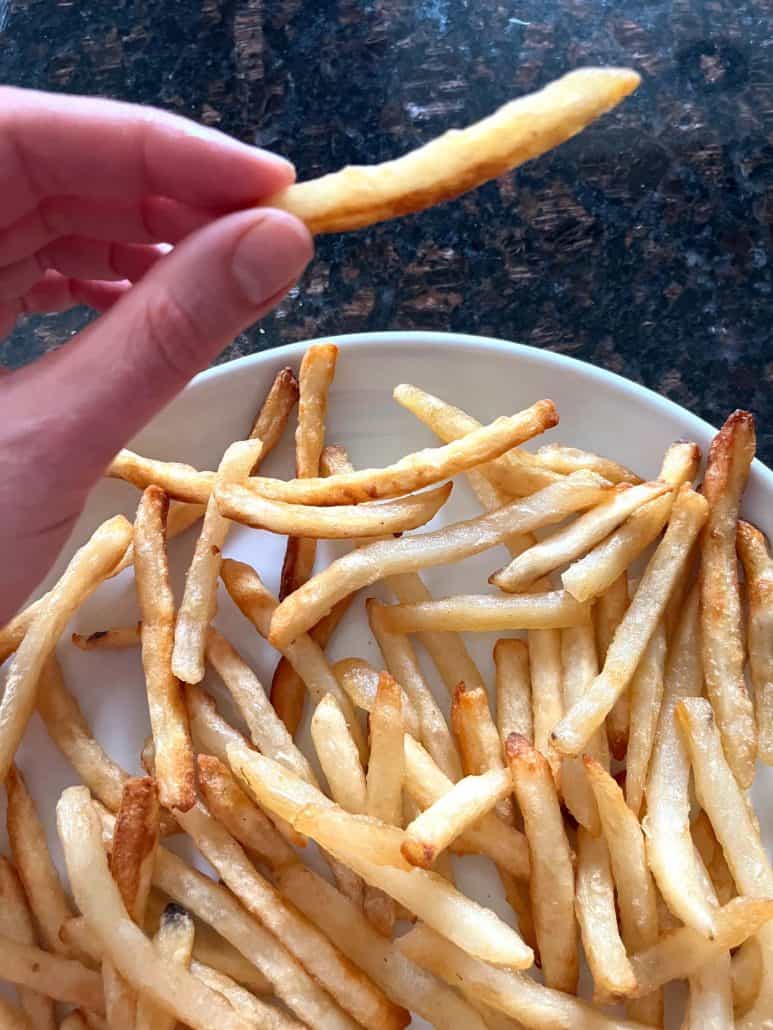 Melanie Mendelson from melaniecooks.com holding a McCain Beer Battered Fry above a plate, showing the golden brown and crispy texture.