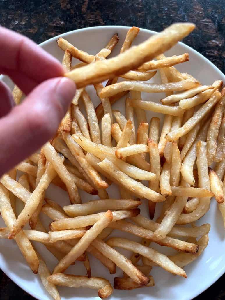 Melanie Mendelson from melaniecooks.com holding a crispy McCain Beer Battered Fry over a plate of fries, showing its perfect texture.